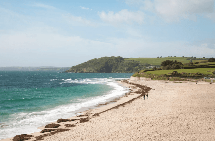 A serene sandy beach with a couple walking their dog in Cornwall